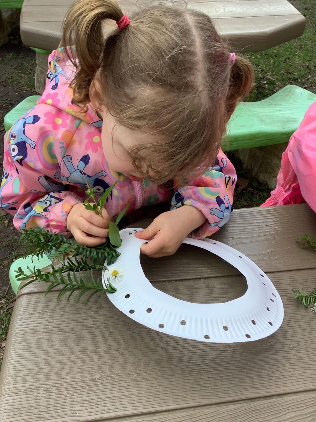 A child threading leaves on a paper plate outdoors