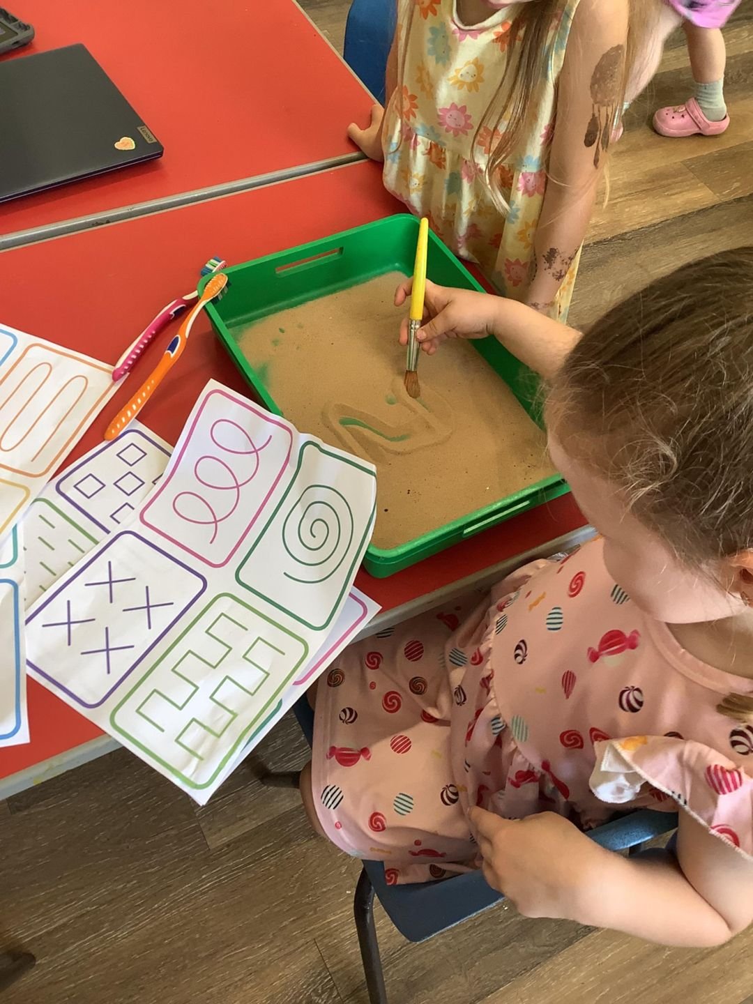 A child practising mark making in a sand tray